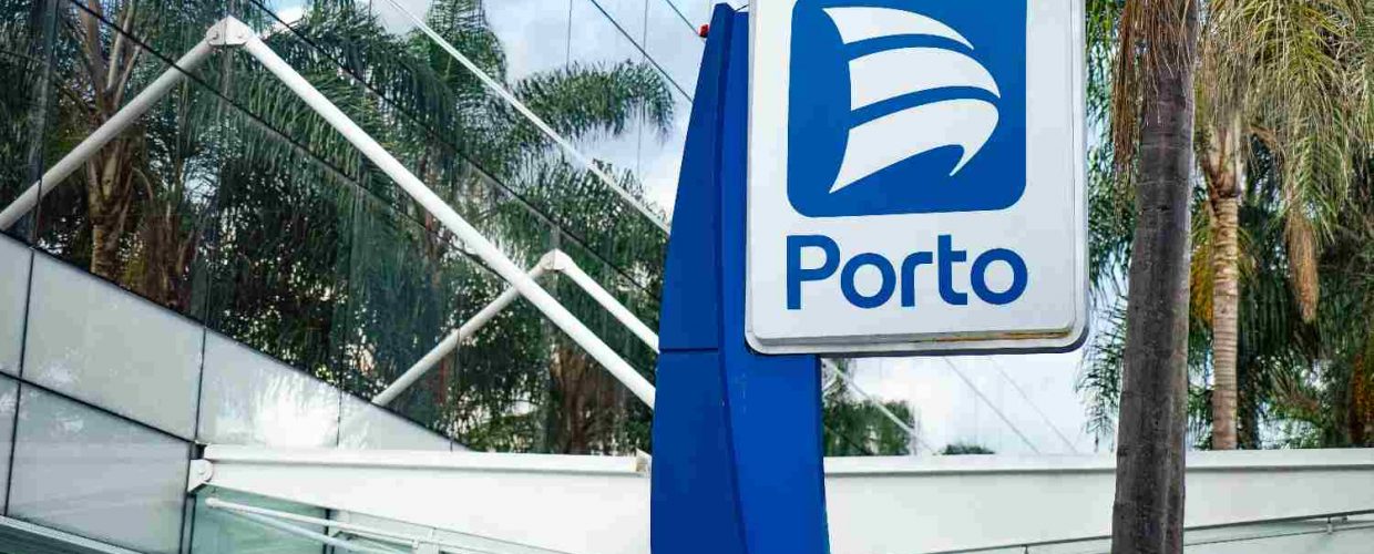 Foto mostra placa com logo da Porto em destaque na frente de um prédio espelhado