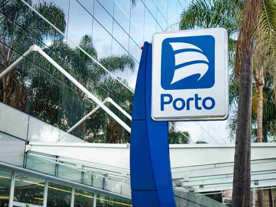 Foto mostra placa com logo da Porto em destaque na frente de um prédio espelhado